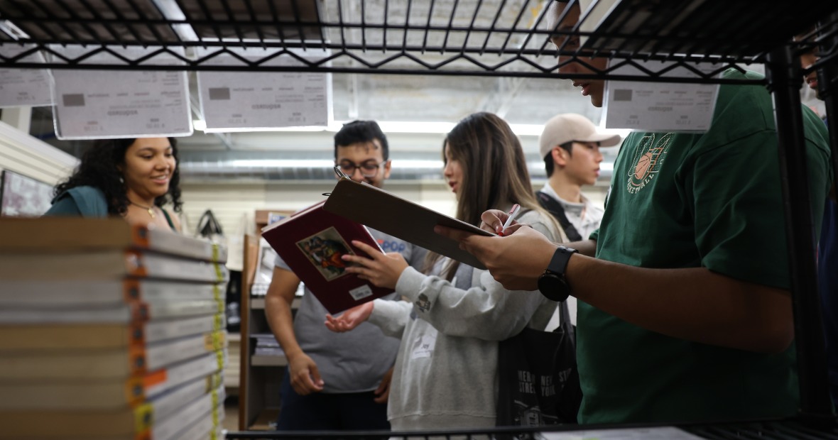 Students chatting and looking at books in the background, with shelf in the foreground
