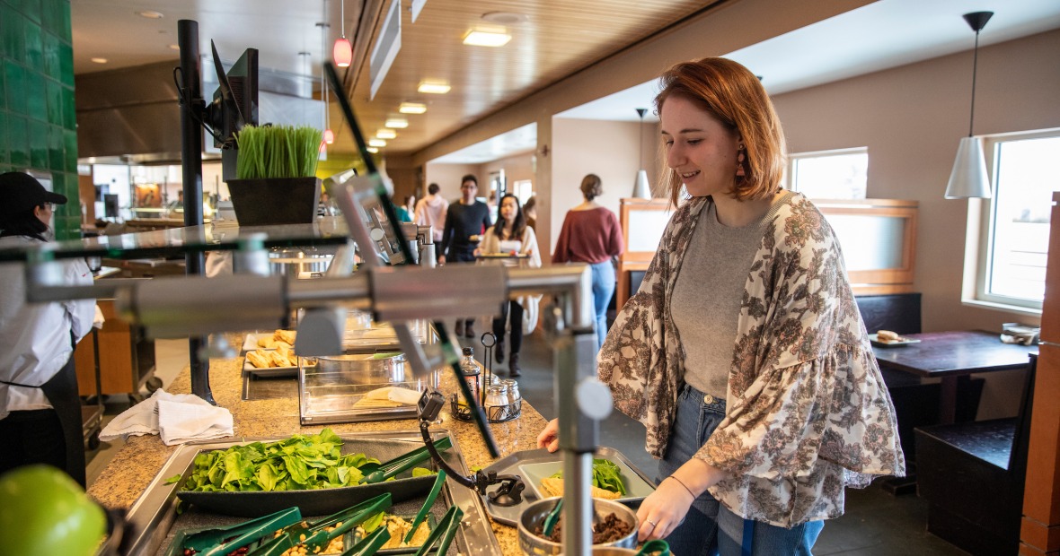 Marnie Monogue stands at a counter with food choices in the dining hall