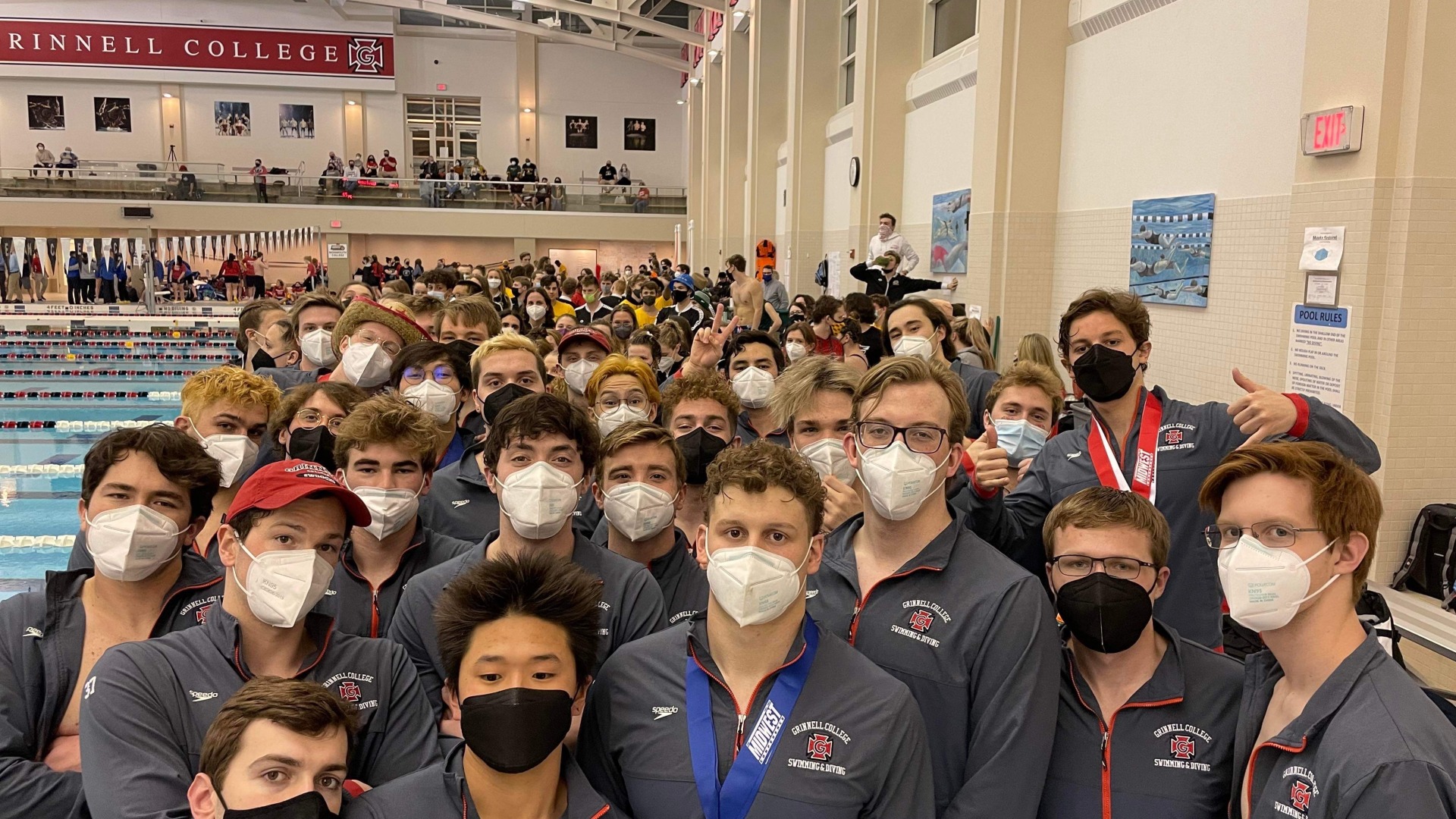 Swim and dive team members all gather together for a casual photo just outside the pool wearing a jacket. There are many members, almost the entire picture is filled with members.