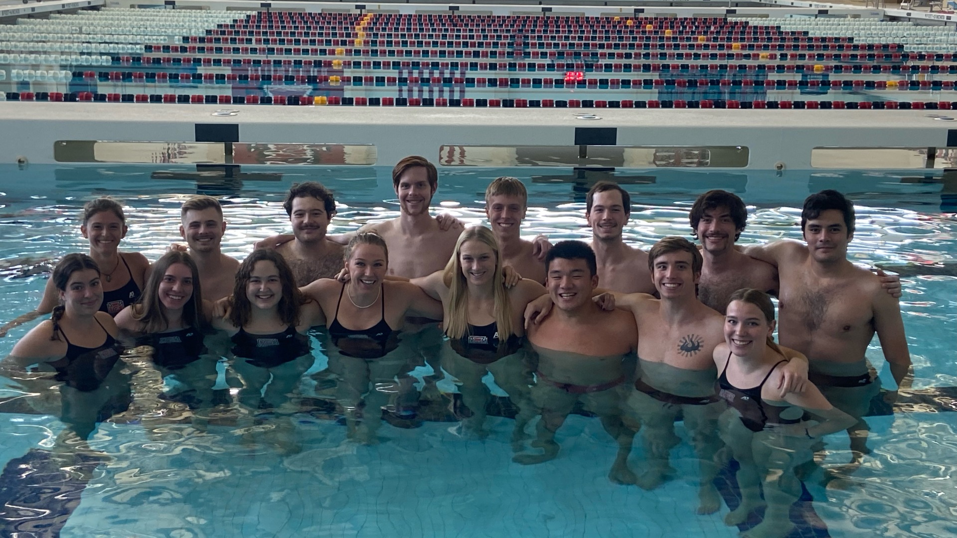 A co-ed swim and dive team gathers inside the pool for pictures. Members all have their hands around each other's shoulders.